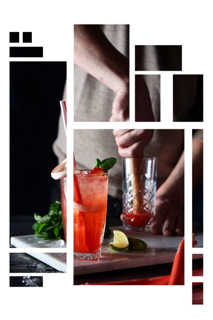 Rød cocktail i forgrunden. I baggrunden står en bartender og er ved at knuse jordbær i et glas