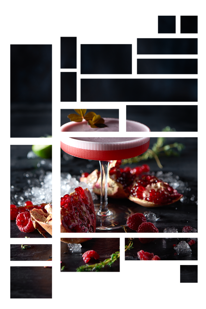 Rød cocktail der står på mørk baggrund. Rundt om ligger hindbær, granatæble og isterninger