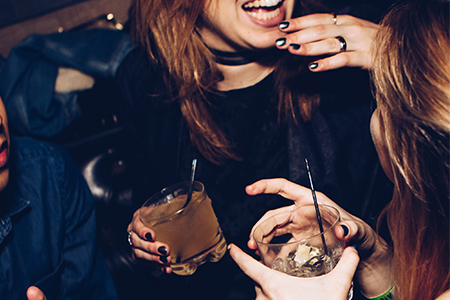 Billede af to mørkhåret piger der holder en cocktail hver med sugerør.